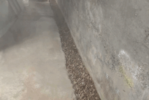 Interior drainage system trench with gravel next to a basement wall, preventing heavy rain on foundations from causing water damage.