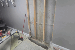 A repaired basement wall with new framing and a drainage trench, fixing cracked concrete and water issues.