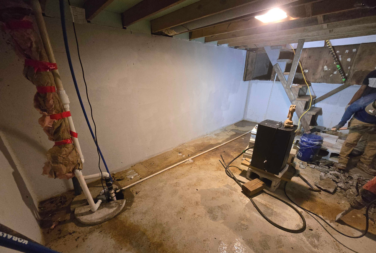 Water stains and small trench in a basement with cracked concrete on the floor, showing moisture issues.